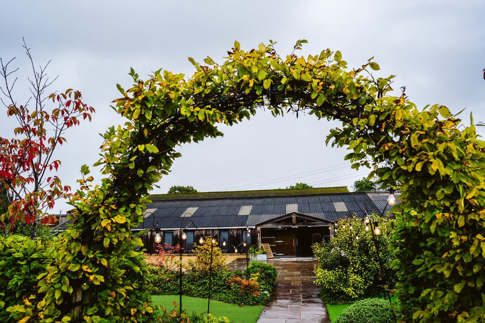 The leafy garden arch at Owen House, framing the path and festoon lights leading to the barn doors